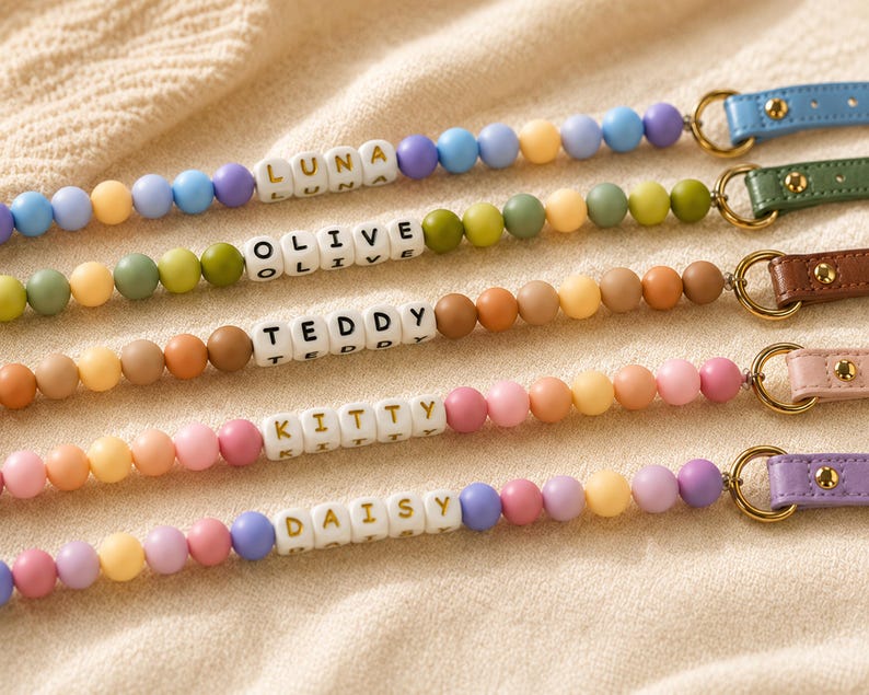 May include: Five personalized beaded lanyards featuring colorful silicone spheres in various pastel and earth tones. Each lanyard includes white letter beads spelling out the names LUNA, OLIVE, TEDDY, KITTY, and DAISY, attached to a leather strap.