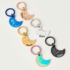 Puede incluir: Una colecci&oacute;n de llaveros en forma de media luna en varios colores, incluyendo azul, oro rosa, oro, plata, negro e iridiscente. Cada llavero presenta un dise&ntilde;o diferente y texto personalizado, como nombres o frases, e incluye un llavero de metal.
