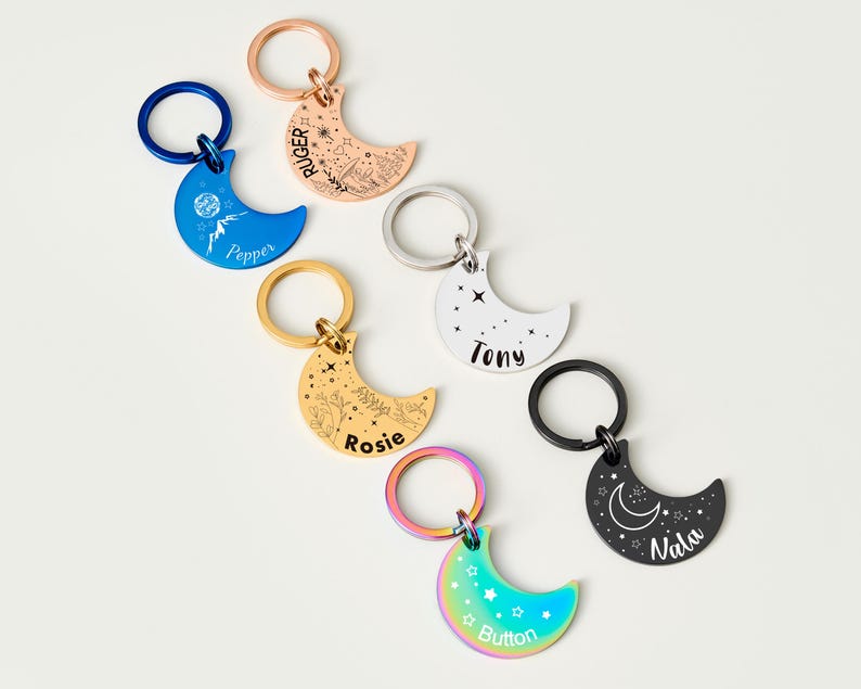 Puede incluir: Una colecci&oacute;n de llaveros en forma de media luna en varios colores, incluyendo azul, oro rosa, oro, plata, negro e iridiscente. Cada llavero presenta un dise&ntilde;o diferente y texto personalizado, como nombres o frases, e incluye un llavero de metal.