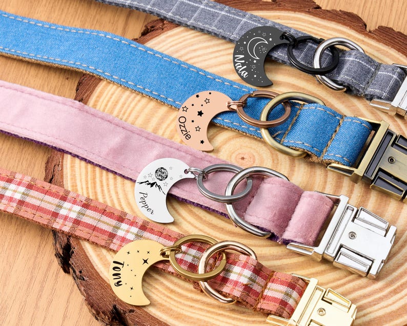Puede incluir: Primer plano de varios collares para perros con etiquetas con forma de media luna. Los collares son de varios colores y patrones, incluyendo mezclilla, cuadros y rosa liso. Cada etiqueta tiene un nombre grabado, como "Nala" y "Tony".
