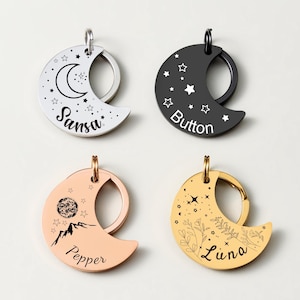 May include: Four crescent moon-shaped pet tags in silver, black, rose gold, and gold. Each tag features a unique design with stars, mountains, or floral elements, and personalized pet names: Sansa, Button, Pepper, and Luna.
