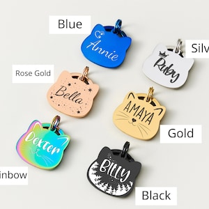 May include: A collection of cat-shaped pet ID tags in various colors, including blue, rose gold, rainbow, gold, silver, and black. Each tag features a different pet's name, such as "Annie," "Bella," "Dexter," "Amaya," "Ruby," and "Billy."