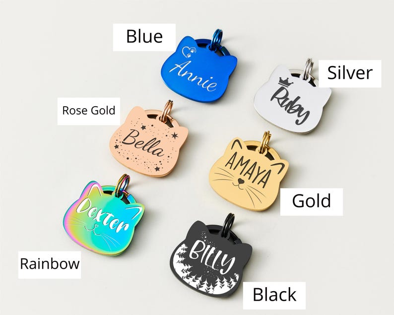 May include: A collection of cat-shaped pet ID tags in various colors, including blue, rose gold, rainbow, gold, silver, and black. Each tag features a different pet's name, such as "Annie," "Bella," "Dexter," "Amaya," "Ruby," and "Billy."