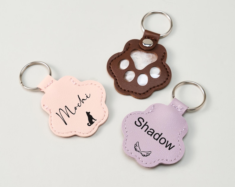 May include: Three paw-shaped keychains in pink, brown, and lavender. The pink keychain has the name "Mochi" and a dog silhouette. The brown keychain has a paw print design. The lavender keychain has the name "Shadow" and angel wings.