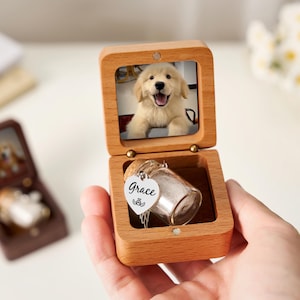 May include: A wooden keepsake box with a photo of a golden retriever puppy inside the lid. The box is open, revealing a small glass vial with a cork stopper and a heart-shaped charm that says "Grace". Another similar box is visible in the background.