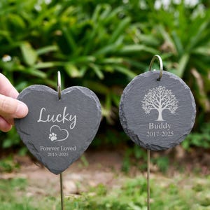 May include: Two slate pet memorial garden stakes. One is heart-shaped with the name "Lucky", a paw print, and "Forever Loved 2015-2025". The other is round with a tree design and the name "Buddy 2017-2025".