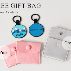 May include: Two round pet tags with black rings, one blue with a mountain design and the name "Dexter", the other blue with a phone number. Also, two pink pouches and a grey pouch with snap closures. Text reads "FREE GIFT BAG" and "2 Colours Available".