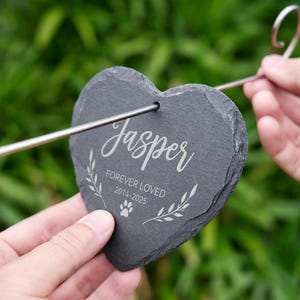 May include: A heart-shaped, dark gray slate pet memorial stake with the name "Jasper" in elegant script. The text "FOREVER LOVED 2014-2025" and a paw print are also engraved. A metal stake is attached for garden placement.