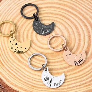 May include: Five crescent moon keychains in gold, black, silver, and rose gold. Each keychain has a ring and is engraved with a name and star or floral designs. The names are "Toffee", "Luna", "Tony", and "Pepper".