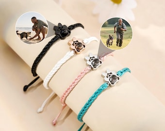 May include: Four braided cord bracelets in black, white, pink, and teal, each with a flower-shaped charm. The charms appear to have a small, round lens in the center. The image also includes two circular photos of people with their pets.