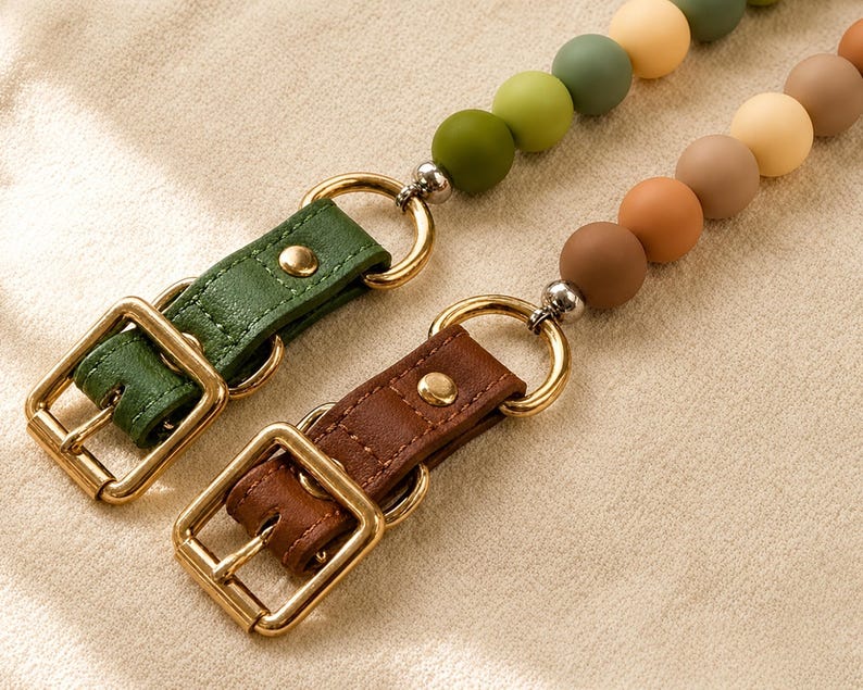 May include: Two lanyards featuring matte silicone beads in shades of green, yellow, and brown. Each lanyard includes a gold-toned metal buckle, a matching ring, and a leather-like strap with a gold-toned rivet, providing a secure attachment point.