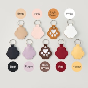 May include: A collection of paw-shaped keychains in various colors, including beige, pink, light brown, white, black, purple, dark brown, red, and yellow. Each keychain has a silver keyring.