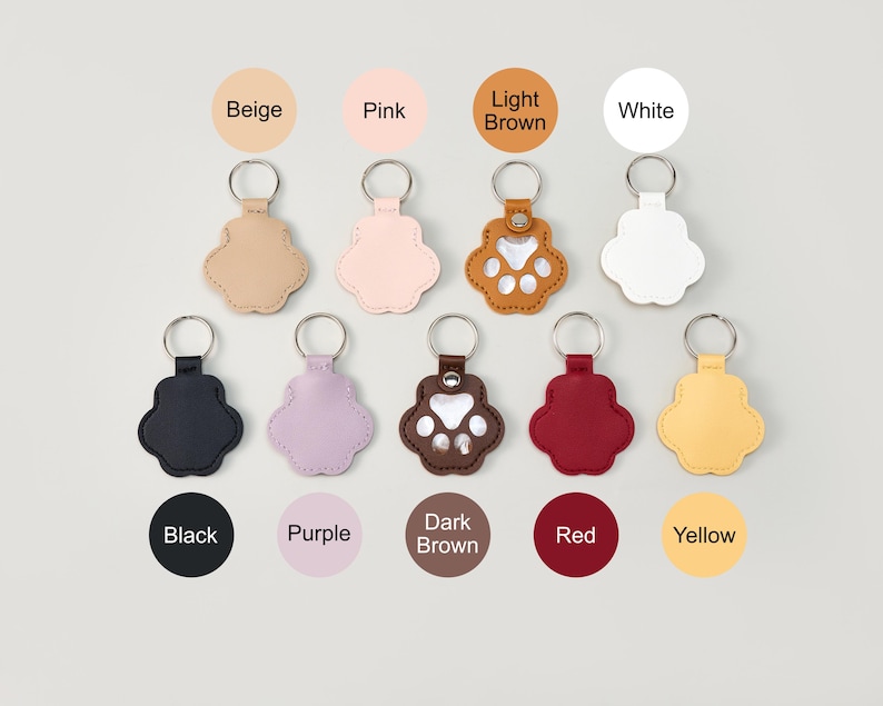 May include: A collection of paw-shaped keychains in various colors, including beige, pink, light brown, white, black, purple, dark brown, red, and yellow. Each keychain has a silver keyring.