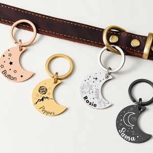 Puede incluir: Cuatro etiquetas para mascotas en forma de media luna en oro rosa, oro, plata y negro, cada una con un llavero. Las etiquetas presentan dise&ntilde;os grabados de estrellas, monta&ntilde;as y patrones florales, con nombres de mascotas como "Button" y "Rosie".