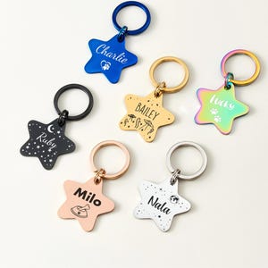 Puede incluir: Colecci&oacute;n de etiquetas de identificaci&oacute;n para mascotas en forma de estrella, en varios colores: azul, negro, dorado, oro rosa e iridiscente. Cada etiqueta presenta el nombre de una mascota y un dise&ntilde;o &uacute;nico.