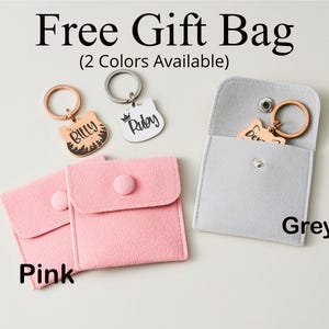 May include: A promotional image featuring cat-shaped keychains with names, presented in pink and grey pouches. The keychains are gold and silver, with the text "Billy" and "Ruby". The image includes the text "Free Gift Bag" and "(2 Colors Available)".