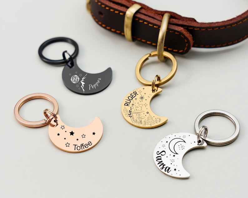 Puede incluir: Cuatro etiquetas para mascotas en forma de media luna en negro, dorado, oro rosa y plateado. Cada etiqueta tiene un dise&ntilde;o y un nombre diferentes, con un collar de perro de cuero en el fondo. Las etiquetas est&aacute;n unidas a llaveros.
