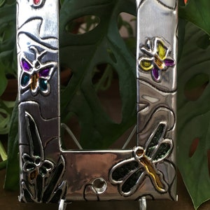May include: A silver metal light switch cover with a decorative border featuring colorful butterflies and dragonflies. The butterflies are yellow, red, purple, and blue. The dragonflies are green, yellow, and orange.