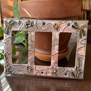 May include: A silver metal light switch cover with a decorative design featuring green and yellow butterflies, flowers, and leaves.