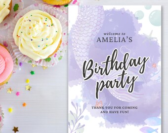 May include: A birthday party sign with the text "welcome to AMELIA'S Birthday party". The sign has a mermaid theme with watercolor accents and decorative elements. Cupcakes with colourful frosting and sprinkles are in the background.