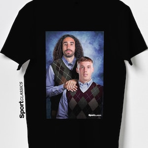 May include: Black t-shirt featuring a portrait of two men wearing argyle vests over button-down shirts. The image has a blue background. The text "Sport Classics" is printed vertically on the left side of the shirt.