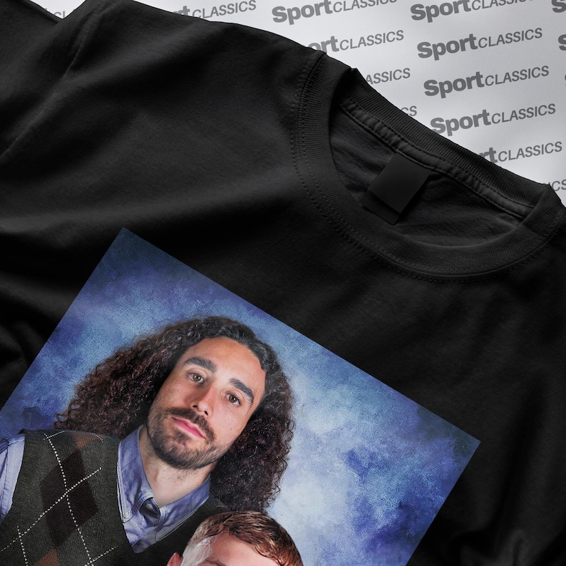 May include: Black crew neck t-shirt with a portrait print. The portrait features two people with curly hair, wearing a sweater vest and a collared shirt. The background is a blue gradient.