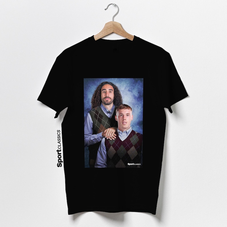 May include: Black t-shirt featuring a portrait of two men wearing argyle vests over button-down shirts. The image has a blue background. The text "Sport Classics" is printed vertically on the left side of the shirt.