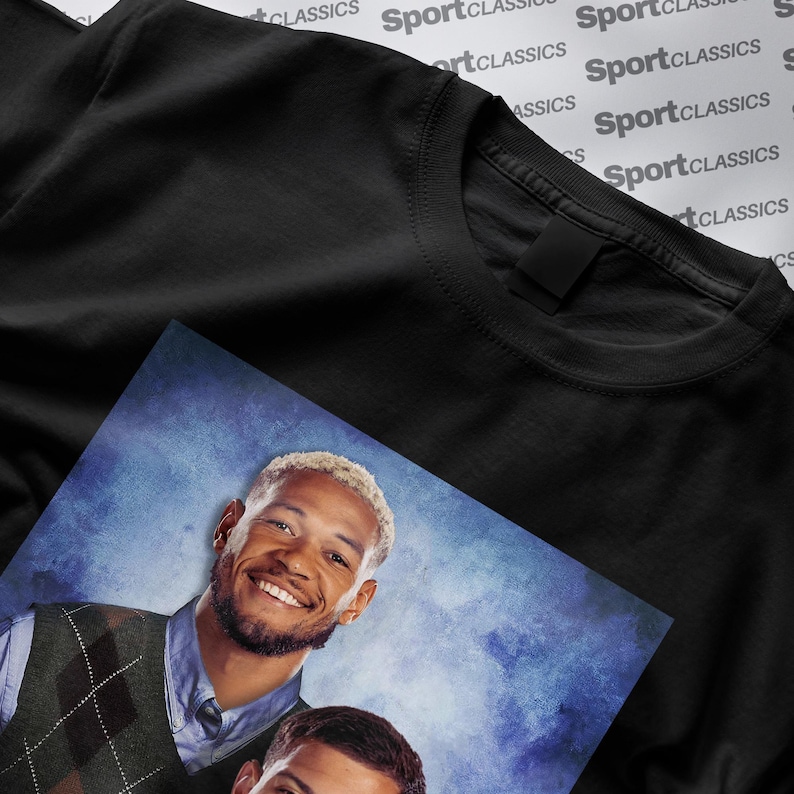 May include: Black crew neck t-shirt with a printed image of two smiling men. The image is on a blue background. The t-shirt is made of a soft material. The background has the words "SportClassics" printed on it.