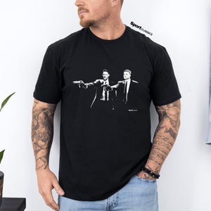 May include: Black t-shirt with a white graphic of two men in suits holding guns. The image is a stylized illustration. The text "SportClassics" is printed at the top right of the shirt.