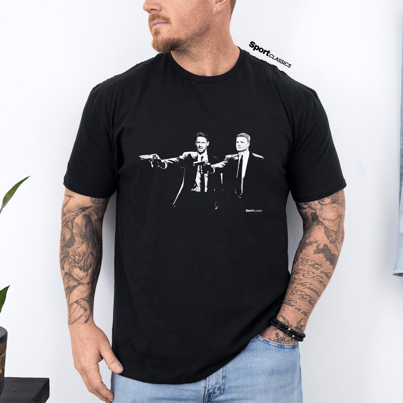 May include: Black t-shirt with a white graphic of two men in suits holding guns. The image is a stylized illustration. The text "SportClassics" is printed at the top right of the shirt.