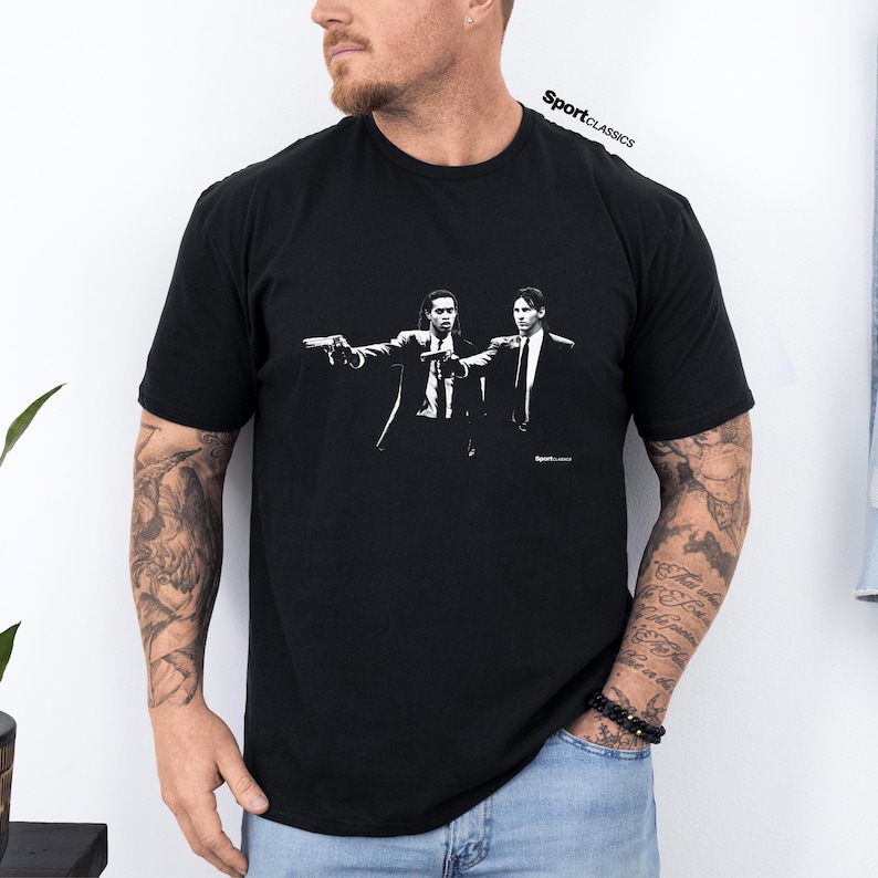May include: Black t-shirt featuring a white graphic of two men in suits holding guns. The text "SportClassics" is printed at the top right. The image is a stylized illustration.