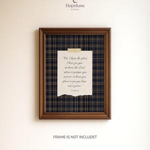 May include: A framed print featuring a quote from Jeremiah 29:11, set against a navy and gold plaid background. The quote is on a torn, cream-colored paper, affixed with tape. The frame is a dark brown color.