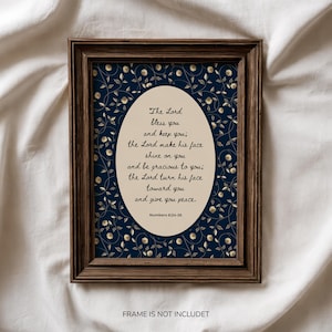 Puede incluir: Un marco rectangular de madera oscura que contiene una impresión con fondo azul marino y un patrón repetitivo de pequeñas flores blancas y enredaderas. Un óvalo central de color crema muestra el texto: The Lord bless you and keep you; the Lord make his face shine on you and be gracious to you; the Lord turn his face toward you and give you peace. Numbers 6:24-26.