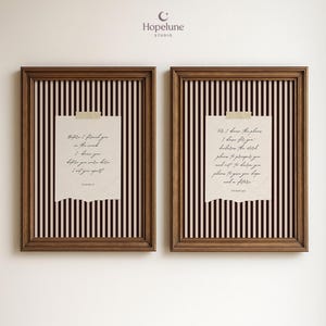 May include: Two framed prints with brown wooden frames. Each print features a torn paper with handwritten text in black ink, set against a black and white striped background. The prints are mounted on a white wall.