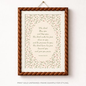 Op de afbeelding: Een rechthoekige wandkunstprint met een crèmekleurig ovaal middenstuk met de tekst The Lord bless you and keep you; the Lord make his face shine on you and be gracious to you; the Lord turn his face toward you and give you peace. Numbers 6:24-26.