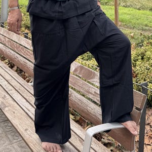 May include: Black loose-fitting trousers featuring a wide-leg silhouette, a high-waisted design with a folded waistband, and a relaxed, flowing fit. The trousers are constructed from a solid black fabric with visible seams and a drop-crotch style.
