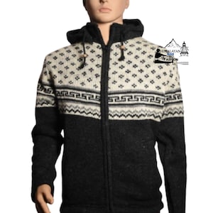 Op de afbeelding: Een hoodie met ritssluiting en een geometrisch patroon in crème en zwart. De trui heeft een zwarte body, een crèmekleurig bovendeel met een herhalend ruitpatroon en een patroonband over de borst. Het Himalayan Soul Fashion-logo is zichtbaar.