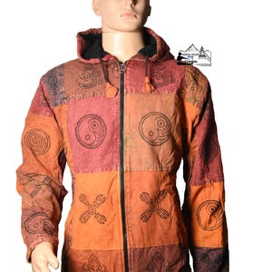 Può includere: Giacca patchwork nei toni dell'arancione, del rosso e del marrone, con cerniera nera e cappuccio. La giacca è decorata con vari simboli spirituali. La giacca è esposta su un manichino.