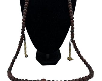 May include: A dark brown beaded necklace displayed on a black mannequin. The necklace features numerous round beads and decorative tassels. The beads appear to be made of wood. The necklace is a religious or spiritual item.