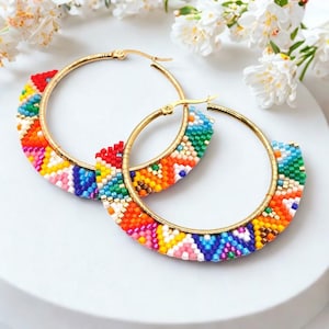 May include: A pair of gold-tone hoop earrings with a colorful beaded design. The earrings feature a vibrant array of colors, including red, orange, yellow, green, blue, and pink. The beaded section is a half-circle shape, adding a unique touch to the classic hoop design.