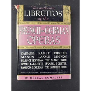 May include: A vintage book cover for "The authentic LIBRETTOS of the FRENCH and GERMAN OPERAS." The cover features a black background with gold lettering and a pink central panel. The book lists 12 complete operas, including Carmen and Faust.