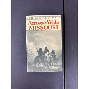 Peut inclure: Un livre intitulé "Across the Wide Missouri" de Bernard DeVoto. La couverture présente une illustration en noir et blanc de trois personnages à cheval. Le titre est en texte rouge et blanc.