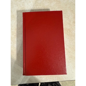 May include: A rectangular book with a solid, vibrant red cover. The front cover is plain and features a textured surface. A vertical spine runs along the left side of the book, which is positioned flat. The book has sharp, clean edges and corners.