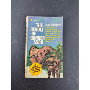 May include: Vintage paperback book titled "The Revolt of Gunner Asch" by Hans Hellmut Kirst. The cover features a blue background with illustrations of soldiers and a wounded man. The book is a Pyramid Books edition.