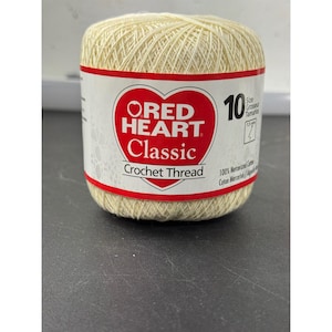 May include: A spool of Red Heart Classic crochet thread in a light beige color. The label features a red heart logo with the text "Red Heart Classic Crochet Thread". The spool is size 10, with a 1.5 mm size.