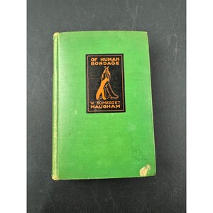 Könnte beinhalten: Ein Vintage-Hardcover-Buch mit dem Titel "Of Human Bondage" von W. Somerset Maugham. Das Buch hat einen hellgrünen Einband mit einer schwarz-orangenen Illustration und Text. Der Einband des Buches ist leicht abgenutzt.