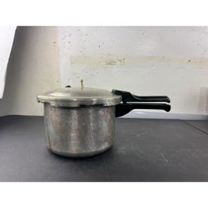以下が含まれることがあります： 黒いハンドルが付いたシルバー色の圧力鍋。 圧力鍋には、小さな通気孔と圧力解放バルブが付いた蓋が付いています。 ポットは暗い表面に置かれています。