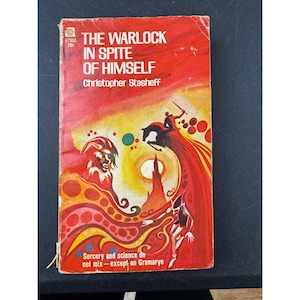 May include: Vintage paperback book titled "The Warlock in Spite of Himself" by Christopher Stasheff. The cover is predominantly red with illustrations of a wizard, a horse, and abstract shapes. The book's cover also includes the text "Sorcery and science do not mix - except on Gramarye."