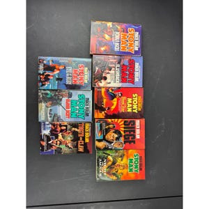 May include: A collection of paperback books featuring the character Stony Man by Mack Bolan. The covers display action-oriented illustrations with titles like "Flashback," "Blood Star," and "Night of the Jaguar." The books are arranged on a dark surface.
