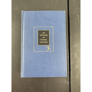 May include: A blue hardcover book titled "AN OUTLINE OF PSYCHO-ANALYSIS" in gold lettering. The book cover features a gold-bordered black rectangle with the title and a small gold figure. The book is closed and in good condition.